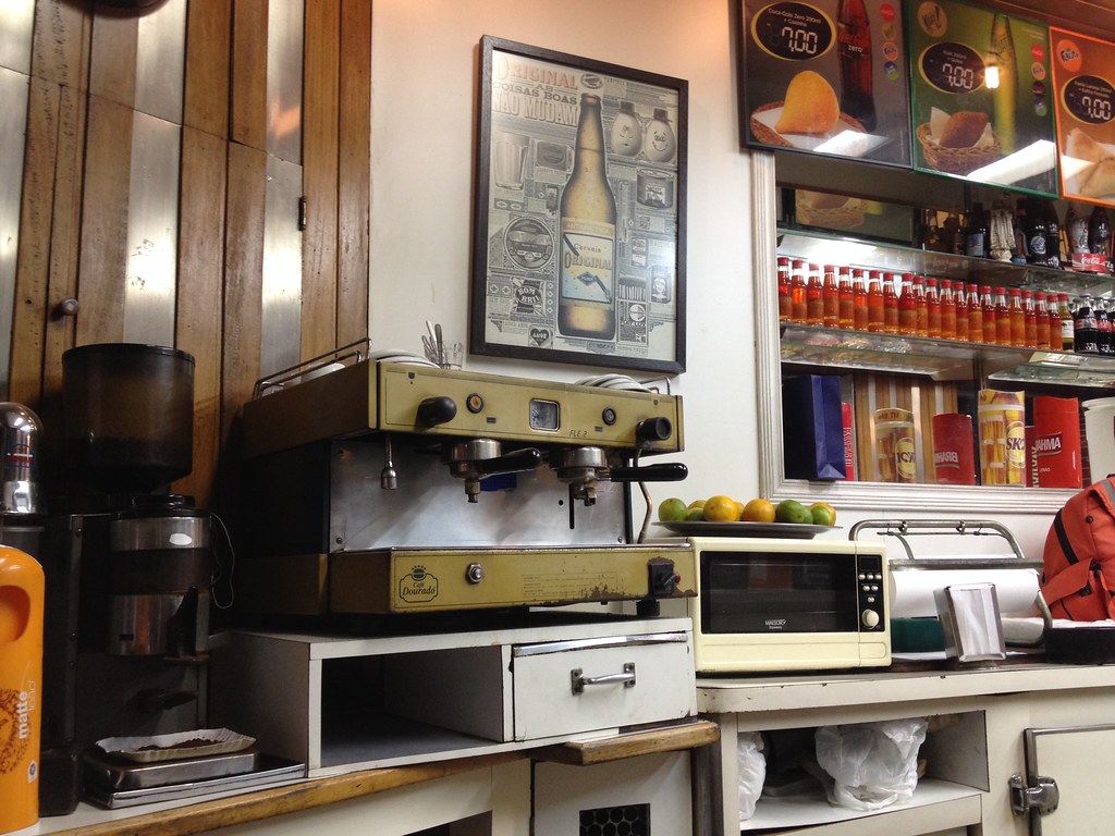 La barra de un bar con una cafetera de palanca y la vitrina de refrescos